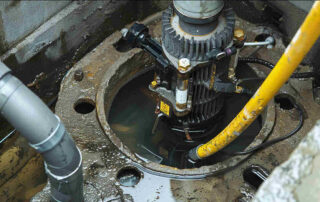 A close-up view of a mechanical sump pump installed in a wet concrete pit filled with murky water.